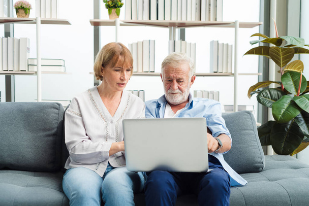 Elderly senior family couple sitting in modern living room together using laptop. Old man get confuse from modern technology. - Zdjęcie, obraz