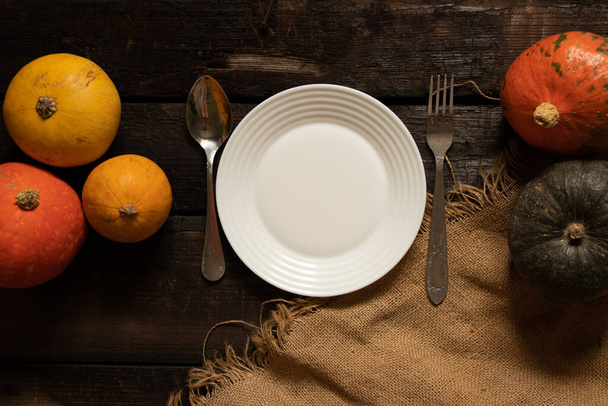 piatto bianco sul tavolo e accanto alle zucche su un vecchio tavolo di legno, arredamento festivo tavolo, piatto sul tavolo - Foto, immagini