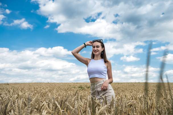 πορτρέτο της νεαρής χαμογελαστής γυναίκας που στέκεται στο χωράφι με το σιτάρι. Ελεύθερη ευτυχισμένη κοπέλα. - Φωτογραφία, εικόνα