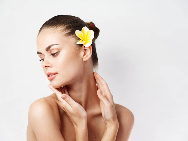 pretty woman with bare shoulders looking towards yellow flower in her hair - Photo, Image