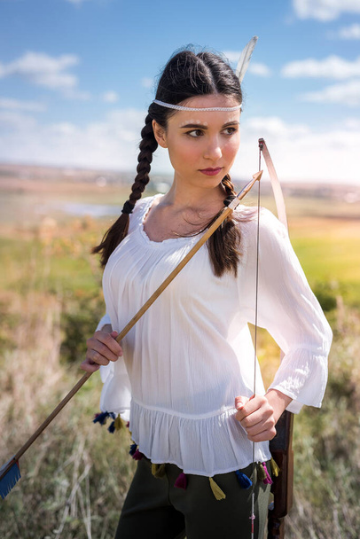 ładna kobieta pozowanie z tradycyjnym stroju i broni jako Indiański wojownik na zewnątrz  - Zdjęcie, obraz