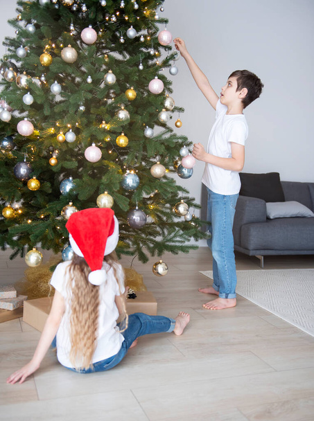 Children - a boy and a girl are playing near the Christmas tree. Living room interior with Christmas tree and decorations. New Year. Gift giving. - Photo, Image
