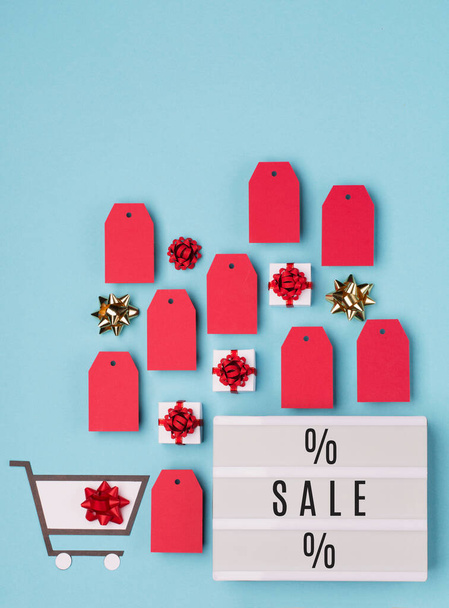 Super Sale day or Singles day concept. Shopping trolley, gift boxes, red tags and white lightbox with text Sale on blue paper background. Online shopping of China. Top view, flat lay, copy space. - Фото, изображение
