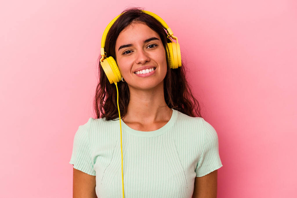Jonge blanke vrouw luisteren muziek geïsoleerd op roze achtergrond gelukkig, glimlachend en vrolijk. - Foto, afbeelding