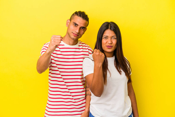 Young latin couple isolated on yellow background showing fist to camera, aggressive facial expression. - Photo, image