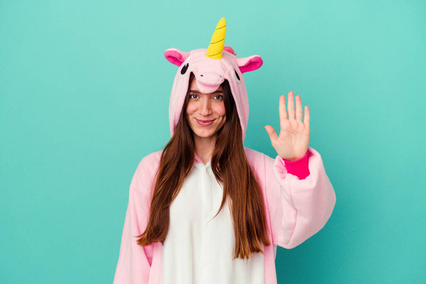 Joven mujer caucásica con un pijama unicornio aislado sobre fondo azul sonriente alegre mostrando el número cinco con los dedos. - Foto, Imagen