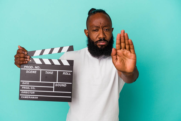 African american man holding clapperboard isolated on blue background standing with outstretched hand showing stop sign, preventing you. - Photo, Image