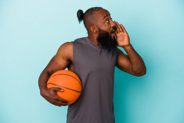 African american man playing basketball isolated on blue background shouting and holding palm near opened mouth. - Foto, Bild