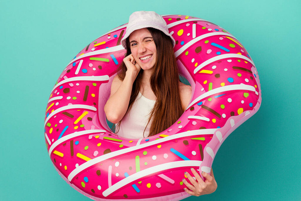 Young caucasian woman with an inflatable donut isolated on blue background covering ears with hands. - Photo, Image