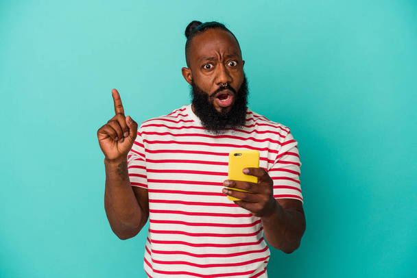 afro-americano homem segurando um celular isolado no fundo azul ter alguma grande ideia, conceito de criatividade. - Foto, Imagem