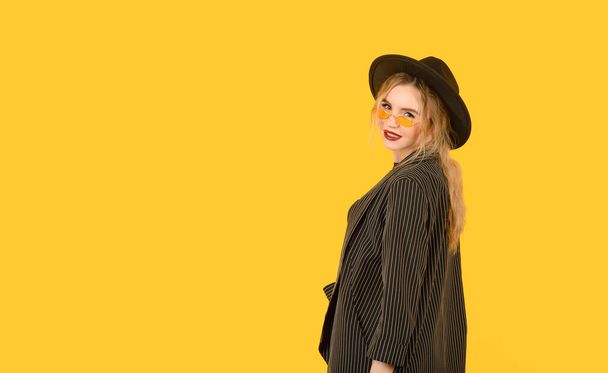 Young girl posing on yellow background half body direct look back side view brown clothes yellow glasses copy space minimalistic - Foto, Imagen