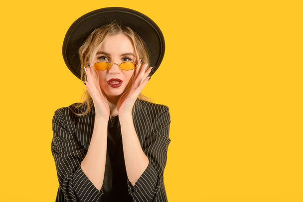 Young girl posing on yellow background direct look mouth hands brown clothes yellow glasses copy space minimalistic - Foto, imagen