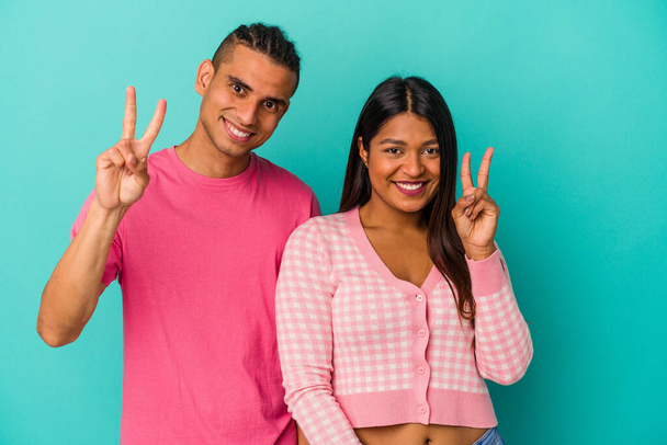 Jovem casal latino isolado no fundo azul mostrando número dois com os dedos. - Foto, Imagem