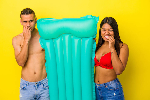 Junge lateinische Paar mit Luftmatratze isoliert auf gelbem Hintergrund beißt Fingernägel, nervös und sehr ängstlich. - Foto, Bild