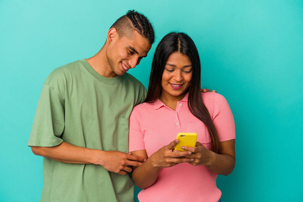 Fiatal latin pár egy mobiltelefon elszigetelt kék háttér - Fotó, kép