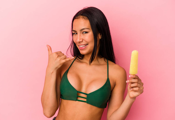 Young Venezuelan woman holding an ice cream isolated on pink background showing a mobile phone call gesture with fingers. - Foto, afbeelding