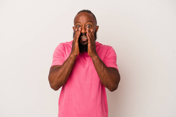 Hombre afroamericano con barba aislada sobre fondo rosa diciendo un chisme, señalando a un lado reportando algo. - Foto, imagen
