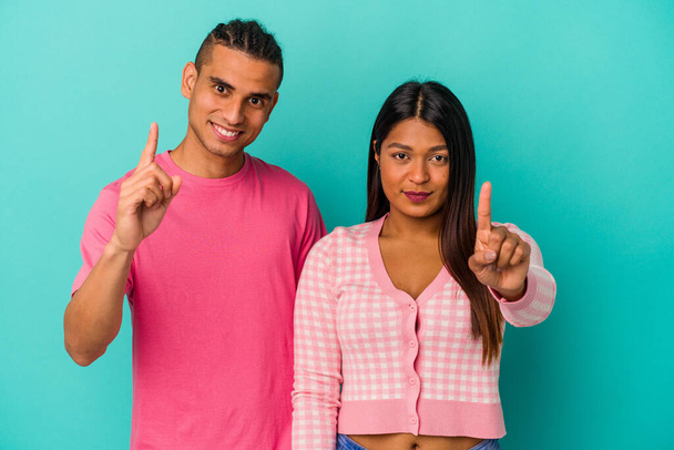 Jovem casal latino isolado no fundo azul mostrando número um com o dedo. - Foto, Imagem