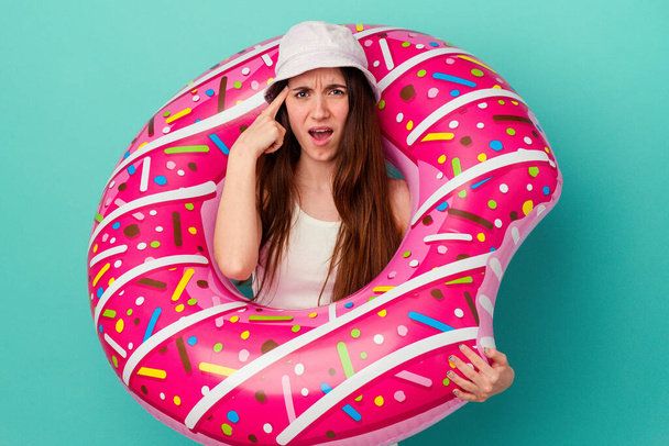 Young caucasian woman with an inflatable donut isolated on blue background showing a disappointment gesture with forefinger. - Foto, Imagem