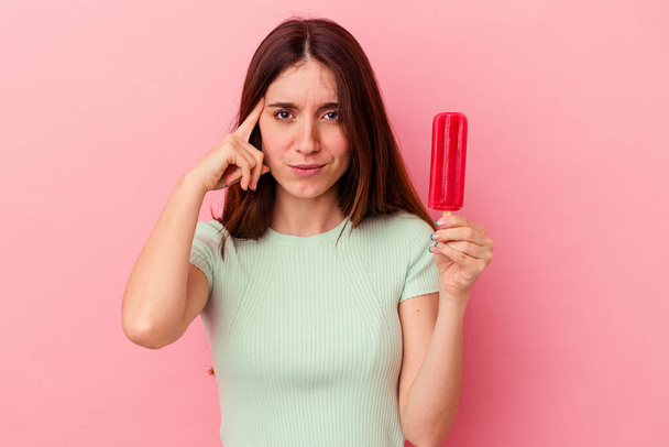 Young caucasian woman holding an ice cream isolated on blue background pointing temple with finger, thinking, focused on a task. - Photo, Image