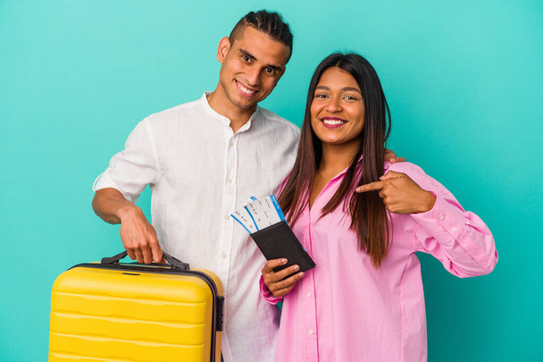 Νεαρό ζευγάρι Λατίνων πρόκειται να ταξιδέψει απομονωμένο σε μπλε φόντο άτομο που δείχνει με το χέρι σε ένα χώρο αντιγραφής πουκάμισο, υπερήφανο και με αυτοπεποίθηση - Φωτογραφία, εικόνα