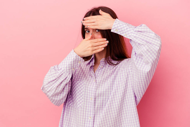 Young caucasian woman isolated on pink background blink at the camera through fingers, embarrassed covering face. - Photo, Image