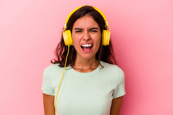 Young caucasian woman listening music isolated on pink background screaming very angry and aggressive. - Photo, Image