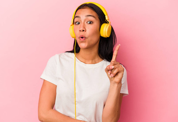 Young Venezuelan woman listening to music isolated on pink background having some great idea, concept of creativity. - Photo, Image