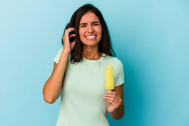 Young caucasian woman holding an ice cream isolated on blue background Young caucasian woman holding an ice cream isolated on blue background covering ears with hands. - Foto, Imagen