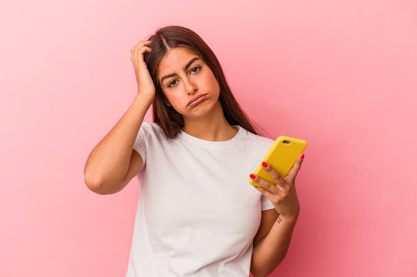 Mladá běloška drží mobilní telefon izolovaný na růžovém pozadí je šokován, ona si vzpomněla na důležité setkání. - Fotografie, Obrázek