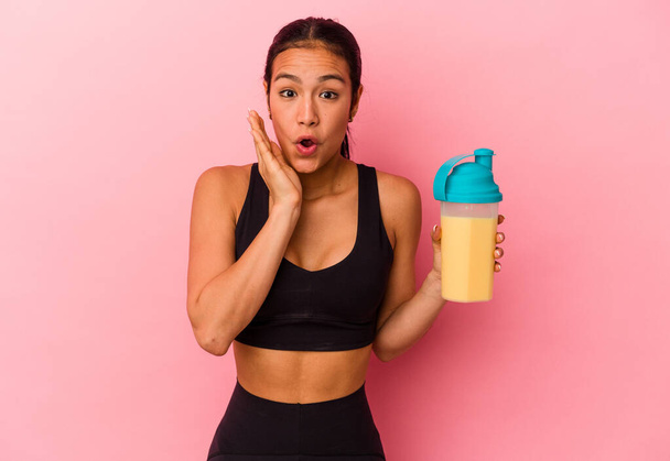 Young Venezuelan woman drinking a protein shake isolated on pink background surprised and shocked. - Foto, Imagem