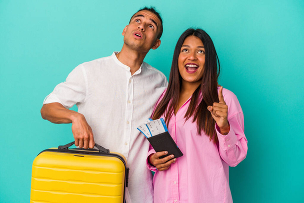 Молодая латинская пара собирается путешествовать изолированно на синем фоне указывая вверх ногами с открытым ртом. - Фото, изображение