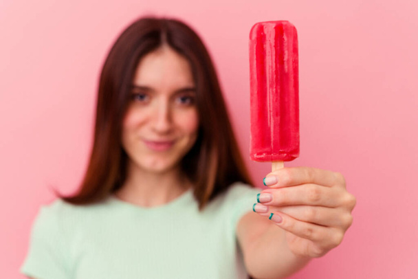 Young caucasian woman holding an ice cream isolated on pink background - Zdjęcie, obraz