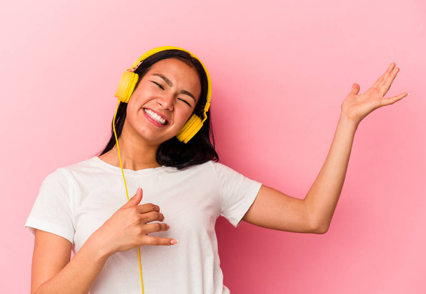 Young Venezuelan woman listening to music isolated on pink background - Foto, imagen