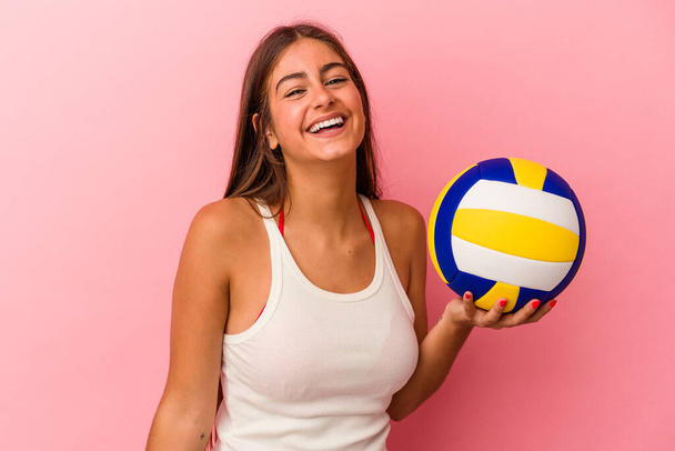 Jonge blanke vrouw met een volleybal geïsoleerd op roze achtergrond lachen en plezier hebben. - Foto, afbeelding