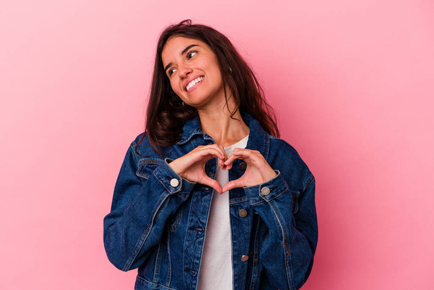 Junge kaukasische Frau auf rosa Hintergrund isoliert lächelnd und zeigt eine Herzform mit Händen. - Foto, Bild