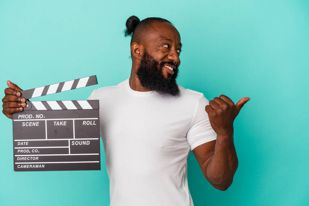 Africký Američan drží clapperboard izolované na modrém pozadí body s palcem pryč, smích a bezstarostný. - Fotografie, Obrázek