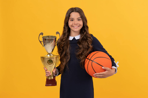 cheerful kid hold basketball ball and champion cup on yellow background, sport success - Photo, Image