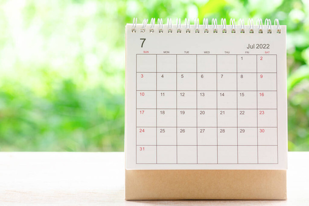 Lipiec miesiąc, Kalendarz biurko 2022 dla organizatora planowania i przypomnienia na drewnianym stole z zielonym tle natury. - Zdjęcie, obraz