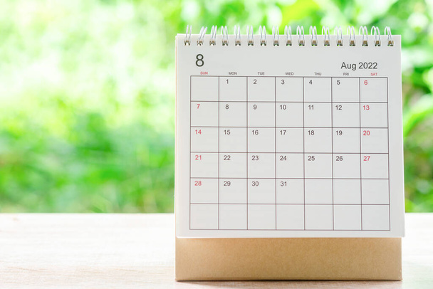 Sierpień miesiąc, Kalendarz biurko 2022 dla organizatora planowania i przypomnienia na drewnianym stole z zielonym tle natury. - Zdjęcie, obraz