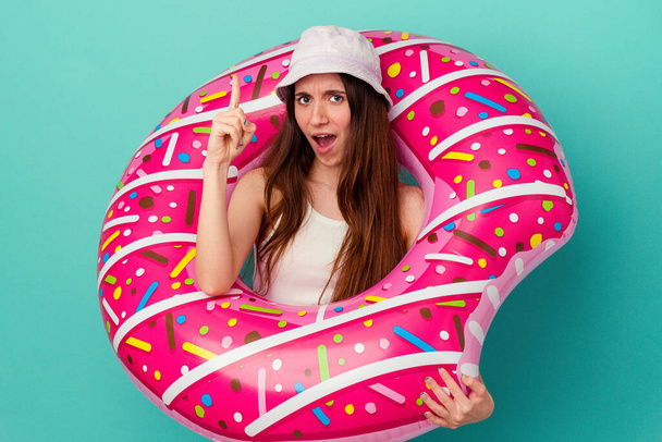 Jonge blanke vrouw met een opblaasbare donut geïsoleerd op blauwe achtergrond met een idee, inspiratie concept. - Foto, afbeelding