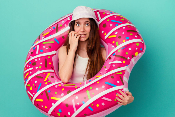 Young caucasian woman with an inflatable donut isolated on blue background biting fingernails, nervous and very anxious. - Fotografie, Obrázek