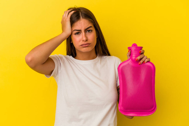 Young caucasian woman holding a hot bottle water isolated on yellow background being shocked, she has remembered important meeting. - Photo, Image