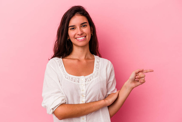 Young caucasian woman isolated on pink background smiling cheerfully pointing with forefinger away. - Photo, Image