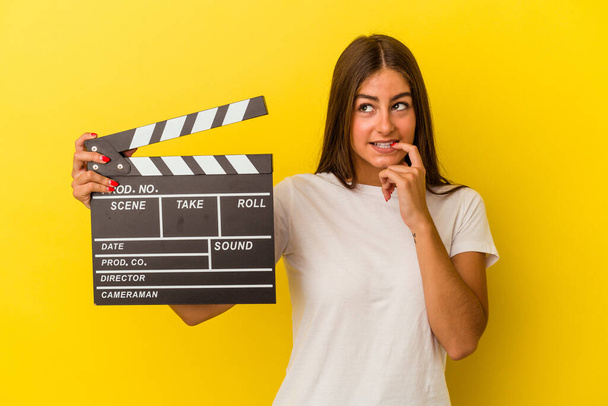 Young caucasian woman holding clapperboard isolated on white background relaxed thinking about something looking at a copy space. - Fotografie, Obrázek