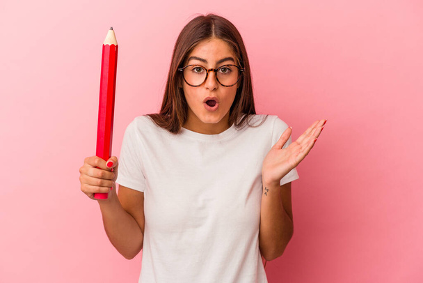 Молодая белая женщина с большим карандашом на розовом фоне удивлена и шокирована. - Фото, изображение