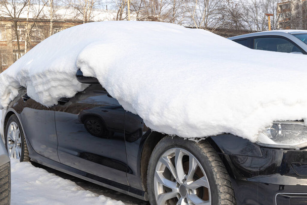 nowy czarny porzucony samochód zimą zaparkowany pod dużą warstwą śniegu w słoneczny mroźny dzień - Zdjęcie, obraz