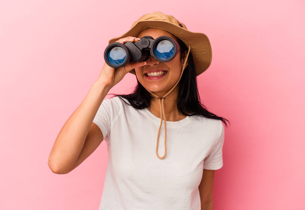 Mujer exploradora de raza mixta joven sosteniendo prismáticos aislados sobre fondo rosa - Foto, imagen