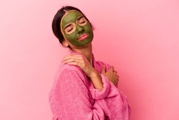 Young caucasian woman wearing a bathrobe and facial mask isolated on pink background - Fotografie, Obrázek