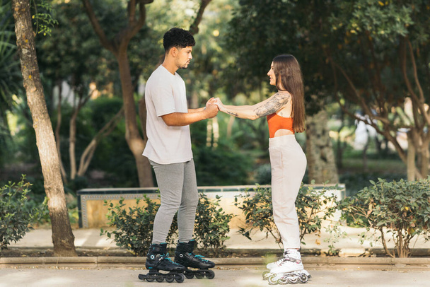 若いカップル一緒に公園でインラインステークスを身に着けて立って - 写真・画像